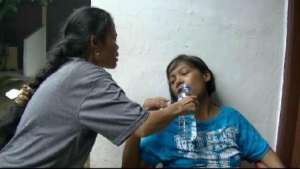salah seorang tetangga tengah memberikan air minum mineral kepada Frida, penderita penyakit ginjal di rumahnya, RT 05/01 Kelurahan Rengas, Ciputat Timur-Kota Tangsel